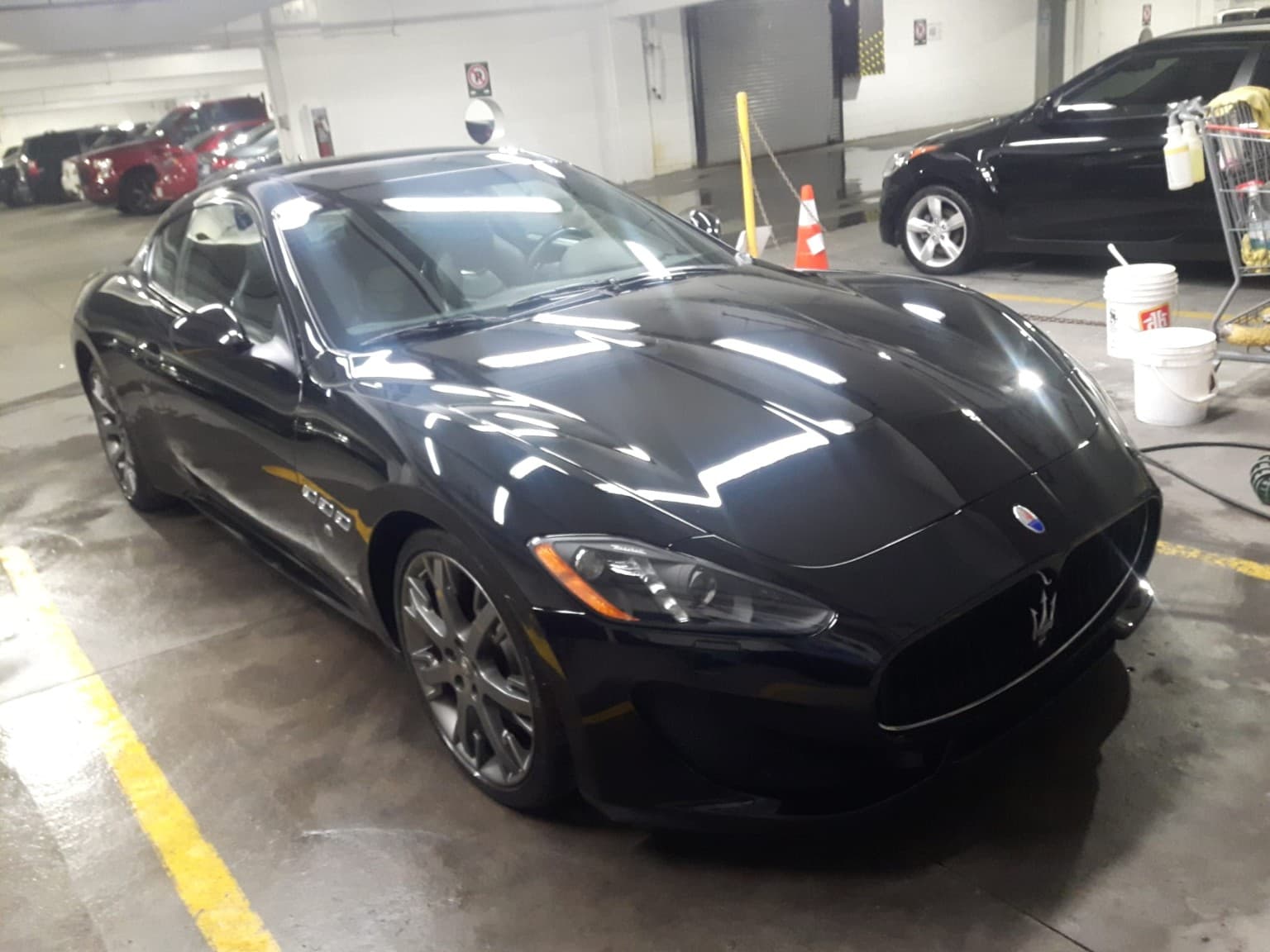 Sleek black Maserati GranTurismo parked in an indoor garage with car wash buckets nearby.